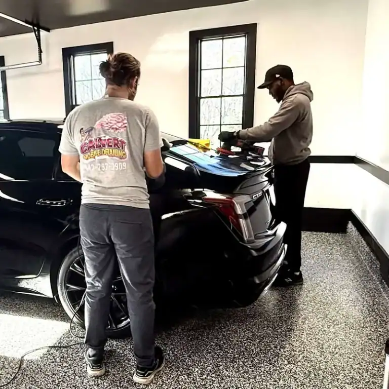 Detailers polishing a black vehicle inside a garage